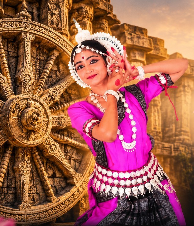 Odissi dancer in a magenta costume and silver temple jewellery holding a graceful mudra before the carved Konark wheel